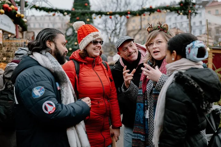 Wooden stalls at a Prague Christmas market with a guide talking to a small group