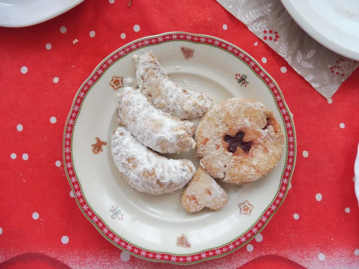 Plate of vanilla crescents and a jam-filled cookie on a Christmas tablecloth