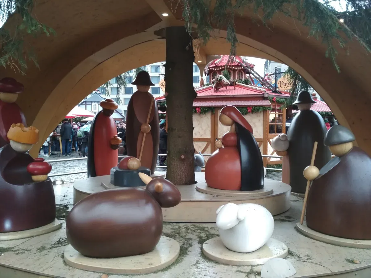Wooden nativity figures inside a Christmas pyramid with Dresden market stalls behind