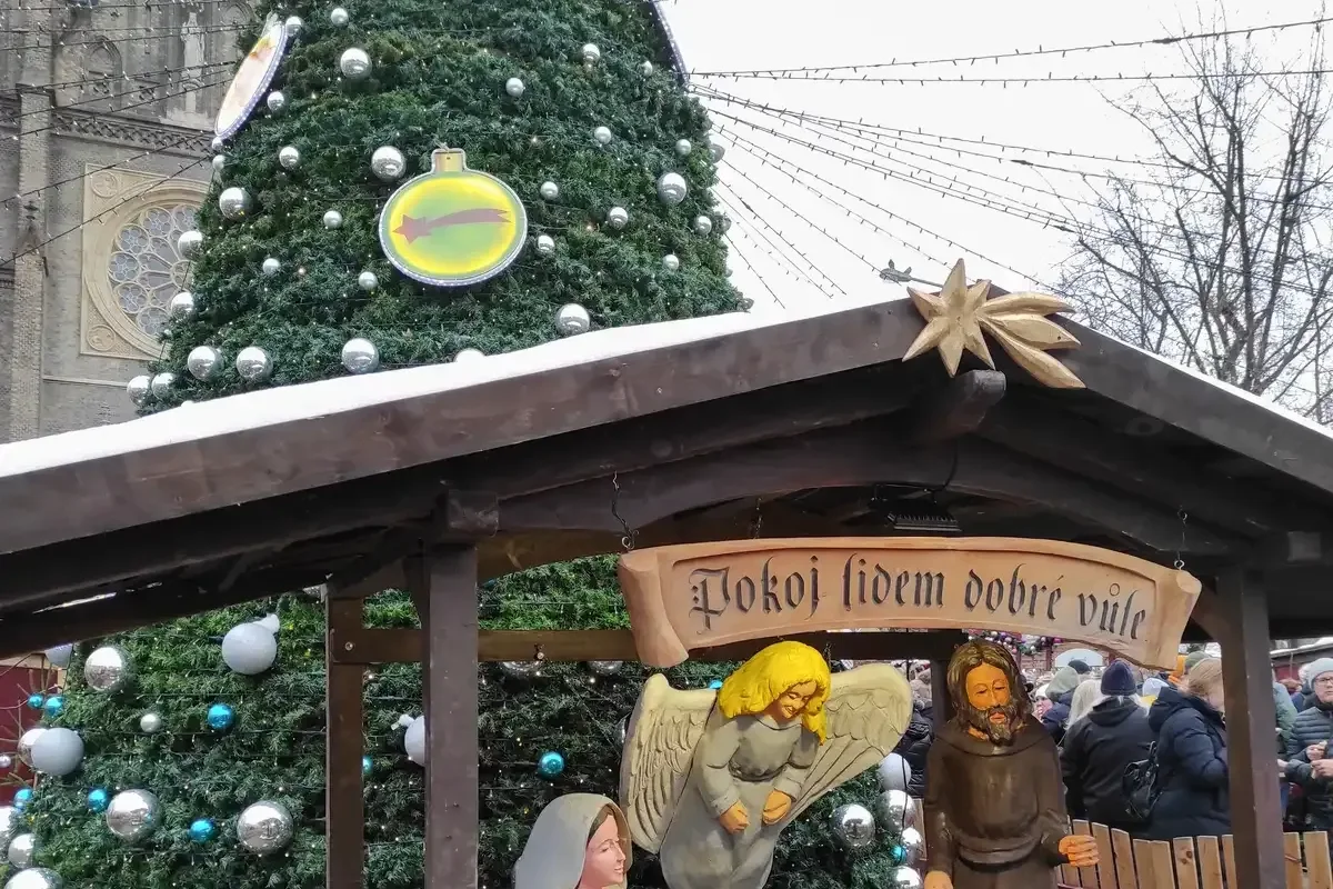 A nativity scene with a straw-roofed stable in front of the decorated Christmas tree at the Náměstí Míru market