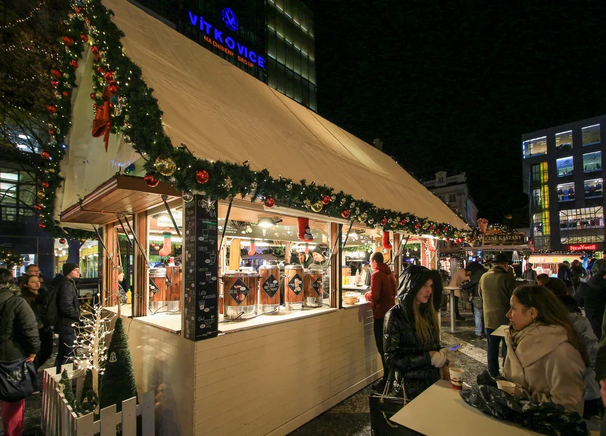 Wooden Christmas market stall with decorated roof and drinks counter at night in Prague